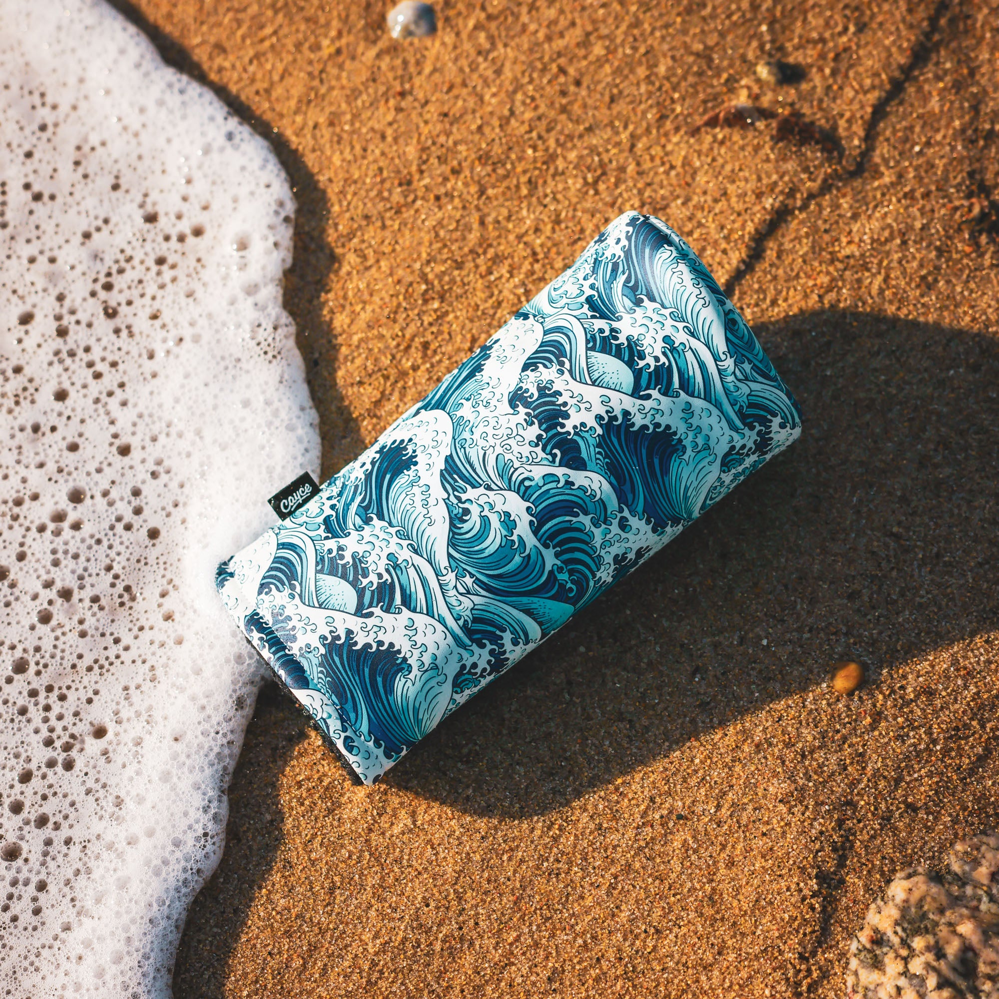 Japanese inspired wave driver headcover laying on the sand with a wave crashing around it