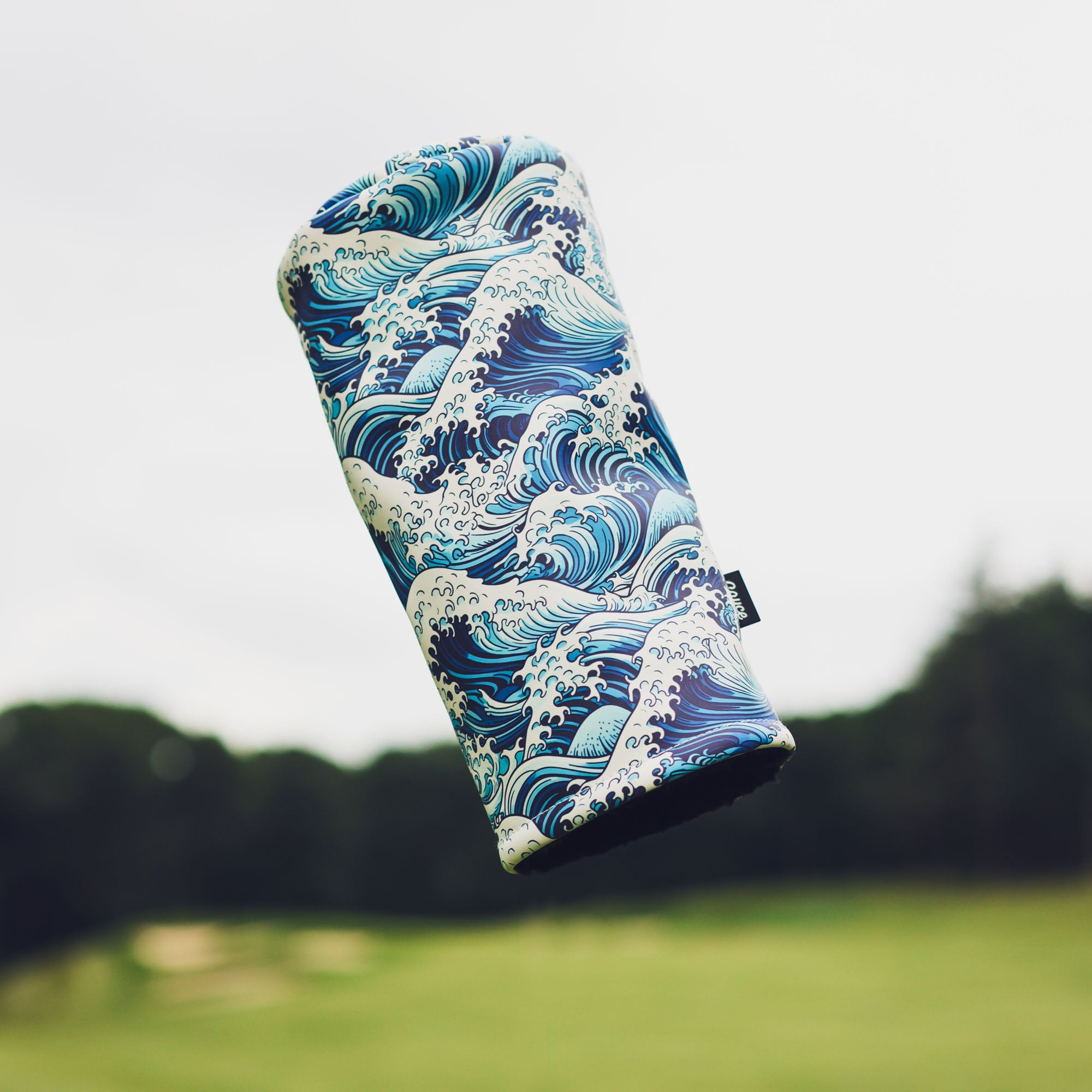 japanese waves driver headcover from cayce golf floating in the air with a blurred out golf course in the background
