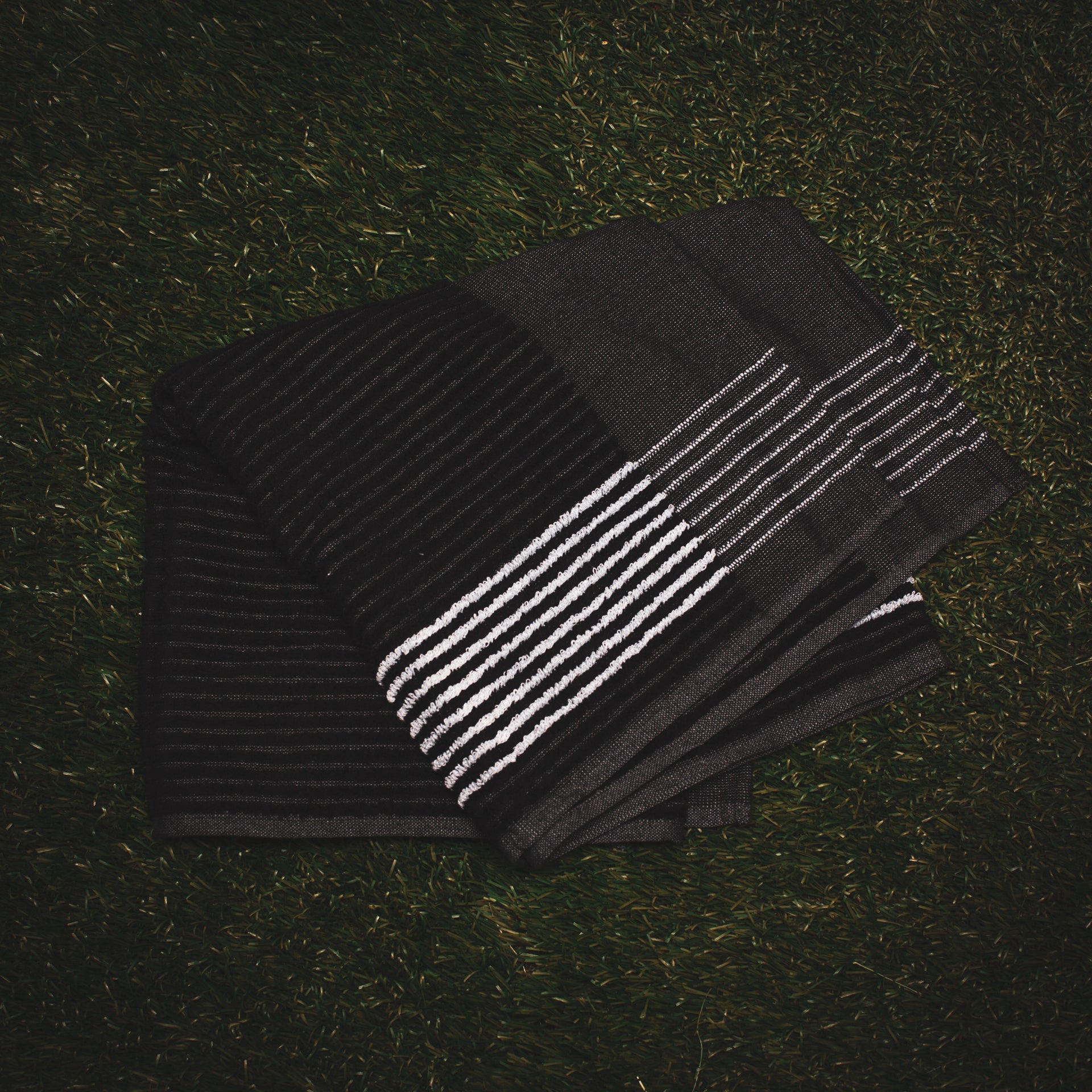 Black Caddy Towel with white stripes from cayce golf laying on the grass (2445375832143)