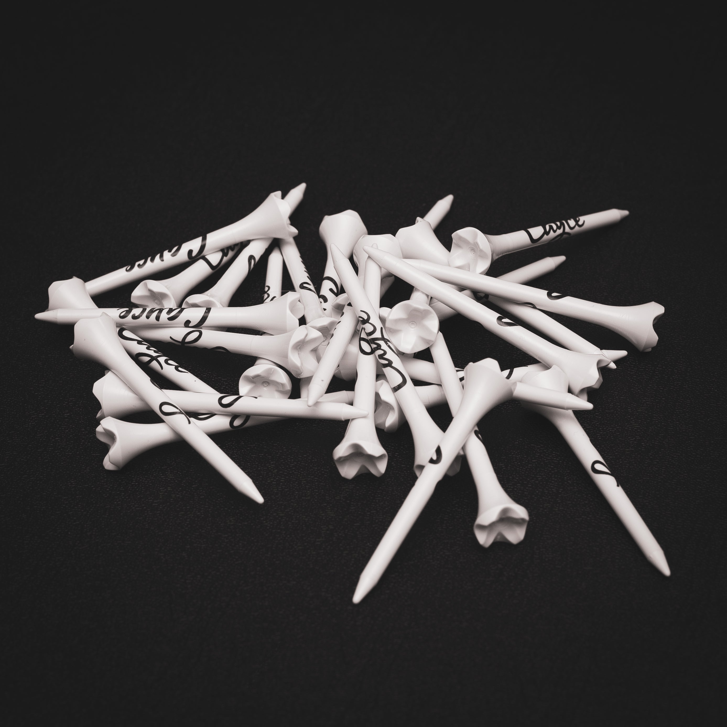 Plastic Performance Golf Tees with Cayce logos in black, stacked in a pile on a black background