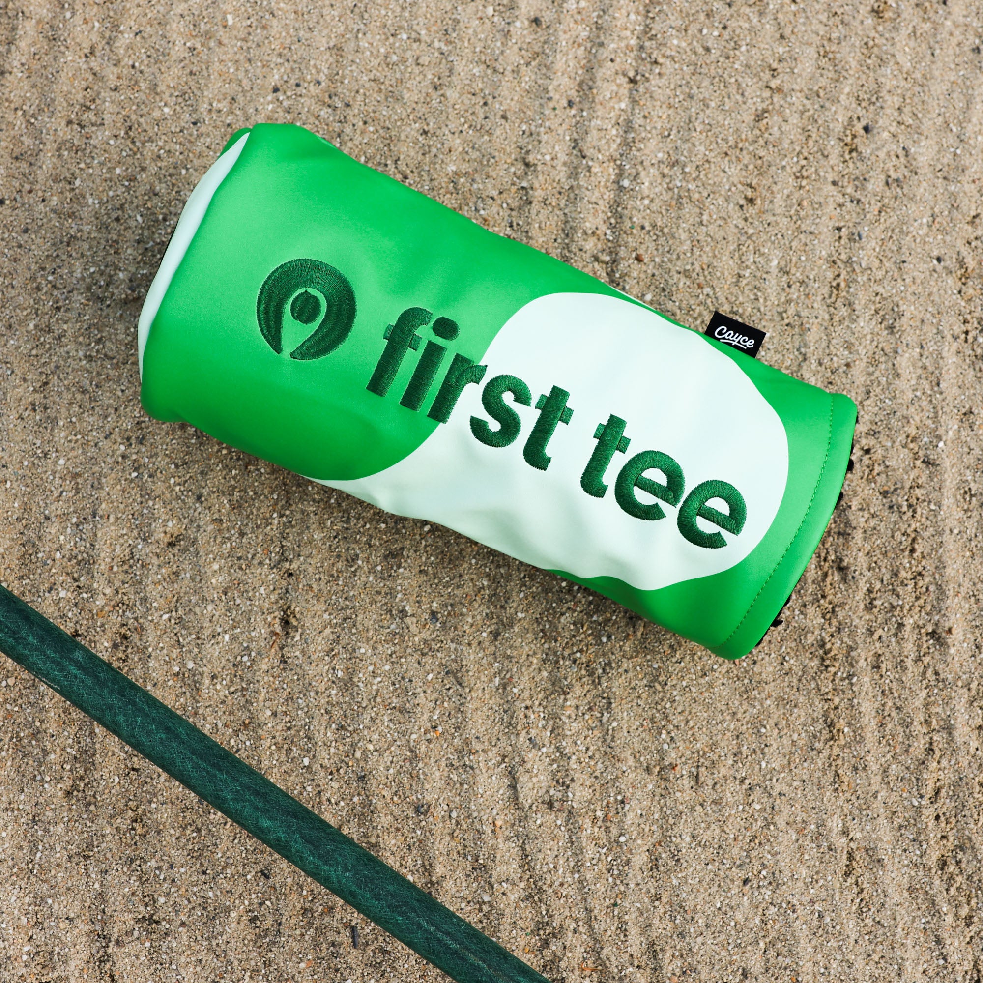 custom barrel-style driver headcover with First Tee branding and colors sitting on a raked bunker surface from Cayce Golf