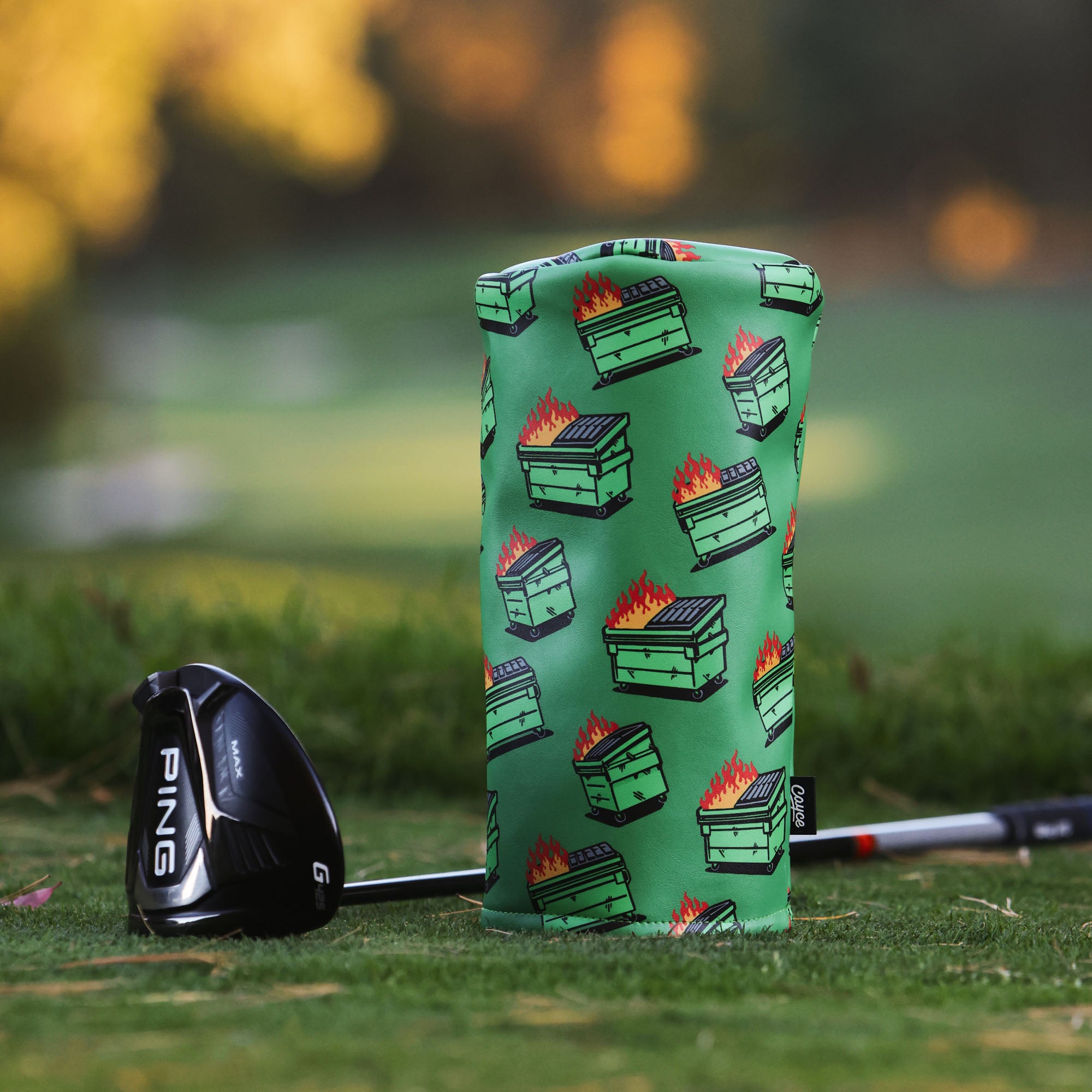 golf club with driver headcover featuring a dancing dumpster fire pattern on a golf course. 
